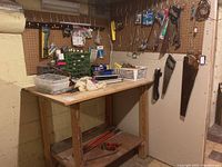 Overview of workbench and pegboard with various hanging tools including saws, hand riveter, and storage bins with hardware items