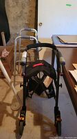 Front view showing stroller with padded black seat and aluminum walker behind it
