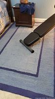 Blue rectangular area rug with multiple shaded rectangular borders in blue, showing texture and calculation of size next to furniture.