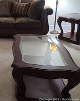Close-up of the coffee table showing the clear glass insert and carved wooden legs with the lower shelf beneath.