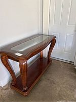 View of wood console table with glass inset top and carved front legs angled near a door.