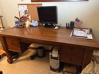 Front full view of solid wood desk showing surface, drawers, wooden legs, and items on top.