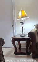 End table with glass insert, carved legs, lower shelf, next to a lamp and couch.