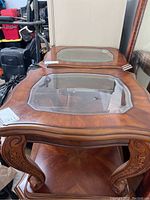 Close-up of two wooden end tables showing the glass inset tops and carved legs