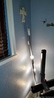 Photo showing the tall metal floor lamp standing next to a wall and exercise equipment, with a visible bulb illuminated.