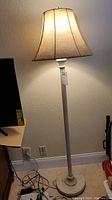 Photo showing the tall floor lamp with light on, featuring a faux stone look lampshade and white base.