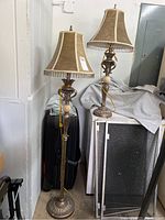 Full view showing two matching lamps: one tall floor lamp and one shorter table lamp. Both have brown leather-like shades trimmed with hanging beads and metal bases with faux marble details.