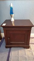 Front view of the wooden side table cabinet with a lava lamp on top, showing overall condition and design.