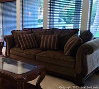 Front view of the brown fabric sofa in living room setting showing three seat cushions and five throw pillows