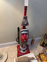 Full view of the red Dirt Devil Featherlite upright vacuum cleaner standing upright on carpet beside a trophy and other household items.