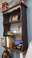 Front view of colonial-style wood wall shelf with various personal items placed on shelves to show scale and function.