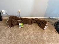 Brown deflated air mattress alongside Coleman Quick Pump battery operated pump box on carpeted floor.