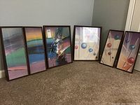 Six abstract art prints in faux wood frames arranged on carpeted floor against wall, showing two sets.