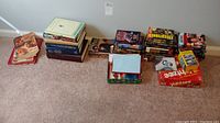 Overview photo of all stacked items including books and games on carpet against wall