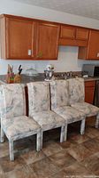 Four fabric dining chairs with abstract pattern upholstery placed in kitchen area against cabinets.