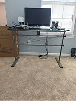 Front view of the glass top desk with metal frame, showing the full desk structure with a monitor and peripherals on top (not included).