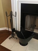 Four metal fireplace tools on metal stand beside a fireplace, showing pineapple-shaped handles and curled feet on stand