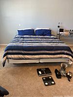Full view of king size bed with blue and white striped comforter and pillows, with body weight scales and wrist braces on floor in front of bed.