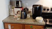 Kitchen counter with GE toaster on original box, Ninja blender, Cuisinart food processor, salad shooter, Keurig coffee maker with glass carafe and accessories.