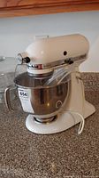 Front and side view of white KitchenAid Artisan stand mixer with stainless steel bowl and splash guard on countertop
