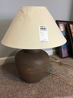 Full view of ceramic lamp showing brown ceramic base with geometric patterns and beige fabric shade with shape damage.