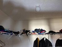 Wide view of wire racks inside a closet with folded men's clothing including shirts and caps.