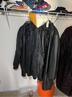 Two black men's leather coats hanging side by side on hangers, showing overall shape and condition.
