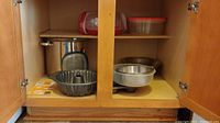Open cabinet showing muffin pans, bundt pan, mixing bowls, plastic containers on shelf above