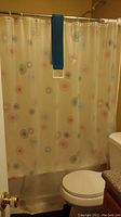 Vinyl shower curtain with multicolored circular flower pattern hanging in bathroom.