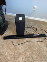 Full view of sound bar and subwoofer on carpet next to a power outlet, showing physical condition and cables.