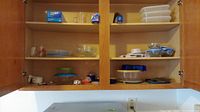 Open wooden cabinet shelves containing assorted plastic and glass storage containers with lids in various sizes and shapes.