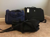 Three suitcases arranged on carpet - blue Revo bag, black Atlantic bag, and black Airway bag in front.