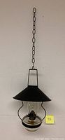 Full view of antique oil lamp chandelier with black tin shade and hanging chain against white wall.