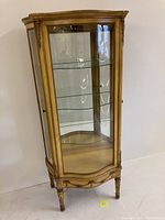 Full front view of giltwood curio cabinet showing three glass shelves and mirrored back