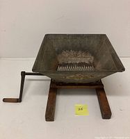 Front view of antique fruit crusher with metal hopper and wooden base, showing hand crank on side.