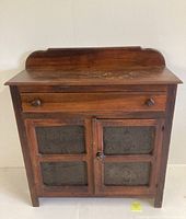 Front view of antique pie safe cabinet showing wood finish, drawer, and punched tin doors.