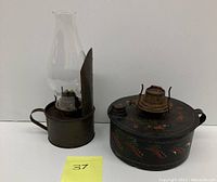 Two antique tin kerosene oil table lamps; one with glass chimney and partial metal reflector, and one with round flat base and hand painted floral decoration.