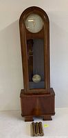 Tall antique Vendetta grandfather clock with oak wood case, visible pendulum, and three weights placed beside it.