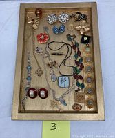Full view of costume jewelry assortment displayed on a wooden tray showing various earrings, bracelets, pendants, and brooches spread neatly.
