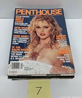 Stack of Penthouse magazines with visible top cover showing a blonde woman in a white outfit, text includes 'Mind Muscle Power' and 'Hemp Honey'.