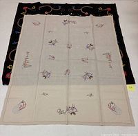 Light-colored needlework tablecloth with Christmas-themed embroidery arranged symmetrically, showing motifs of snowmen, bells, birds, and Christmas trees.