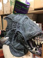 Front view of grey detailed alien monster latex mask with teeth and tag reading 'Alien Monster Mask'.