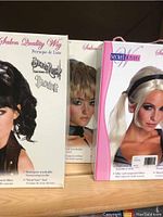 Photo of three boxed wigs featuring different styles: a black curly wig, a short blonde wavy wig, and a blonde wig with pigtails.