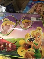 Box showing Disney TinkerBell felt wig for children with yellow wig and green decoration.