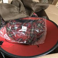 Photo of several hats including a wide-brim brown hat and a red plaid hat in clear plastic packaging, inside a cardboard box.