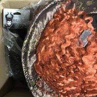 Photo of Mad Hatter hat with curly orange hair and patterned top hat base in box along with other hats