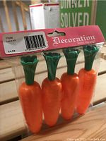 Four plastic carrot-shaped decorations in original packaging with pink header card labeled 'Decoration' and barcode.
