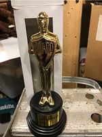 Gold colored standing award statue with 'Award' shield on round black base, placed next to white packaging box