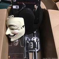 Open box shows deluxe black hat, white Guy Fawkes mask, and packaged costume accessories for V for Vendetta