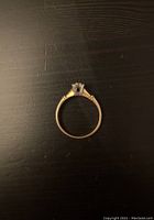 Photo of the ring laid flat showing the band and the profile of the prong setting holding the clear stone.